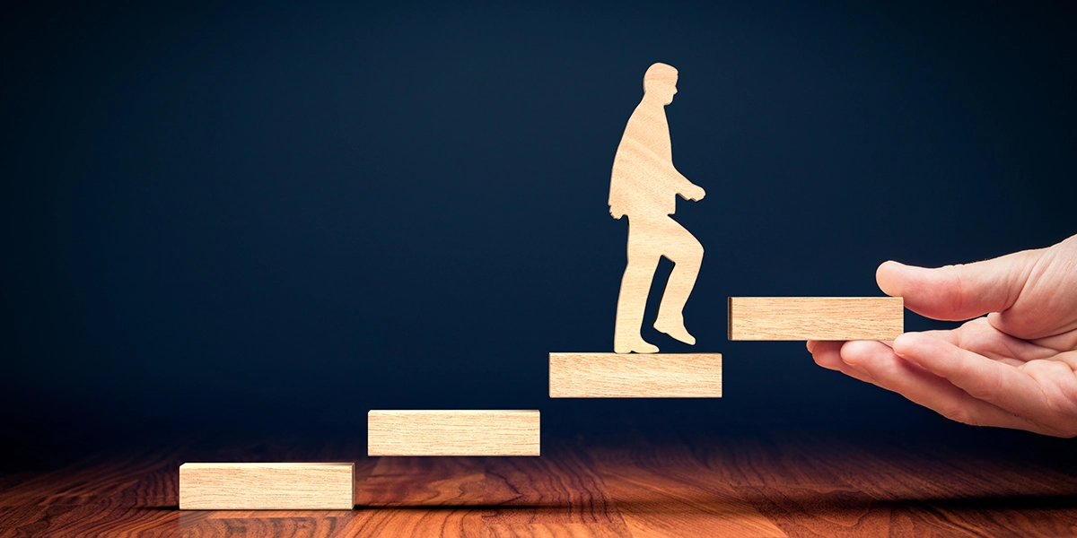 A hand guiding a wooden figure upwards, symbolising leadership progression and development.