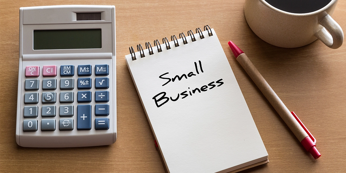 A calculator, notepad, and pen on a desk symbolise essential tools used in financial planning for small businesses.