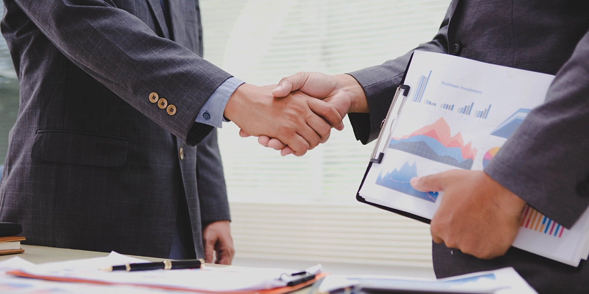 Switching Accountants shown by two professionals shaking hands with financial charts, symbolising a smooth transition.