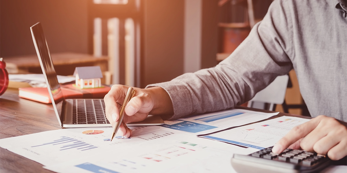 Accountant analysing financial reports and using calculator to illustrate the value of outsourcing accounting functions.