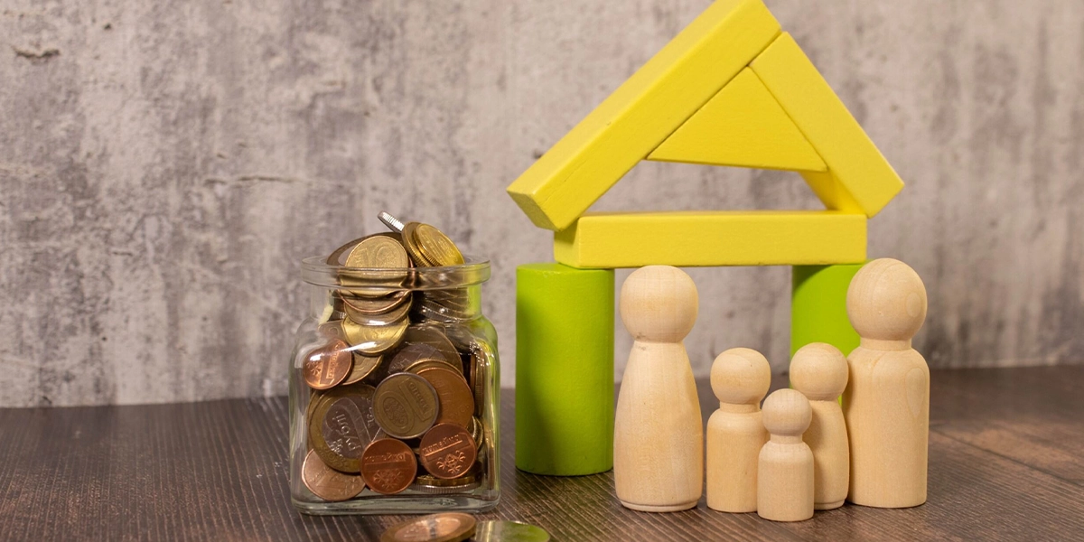 Glass jar of coins beside wooden family figures and a toy house, representing Inherited Assets Tax Planning in the UK.