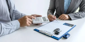 A person calculating VAT on Car Hire with a rental agreement, car keys, and a calculator on the desk.