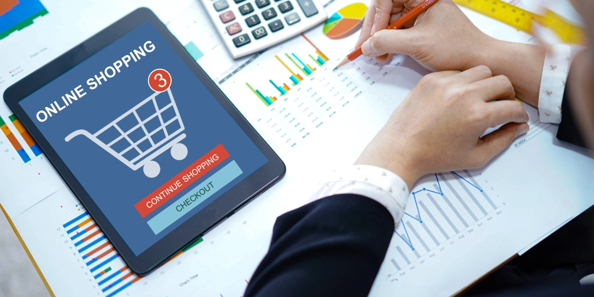 Hands reviewing sales graphs alongside an online checkout screen, illustrating Deemed Reseller Rules.